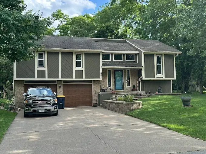 A green house with a grey roof & truck parked in the driveway