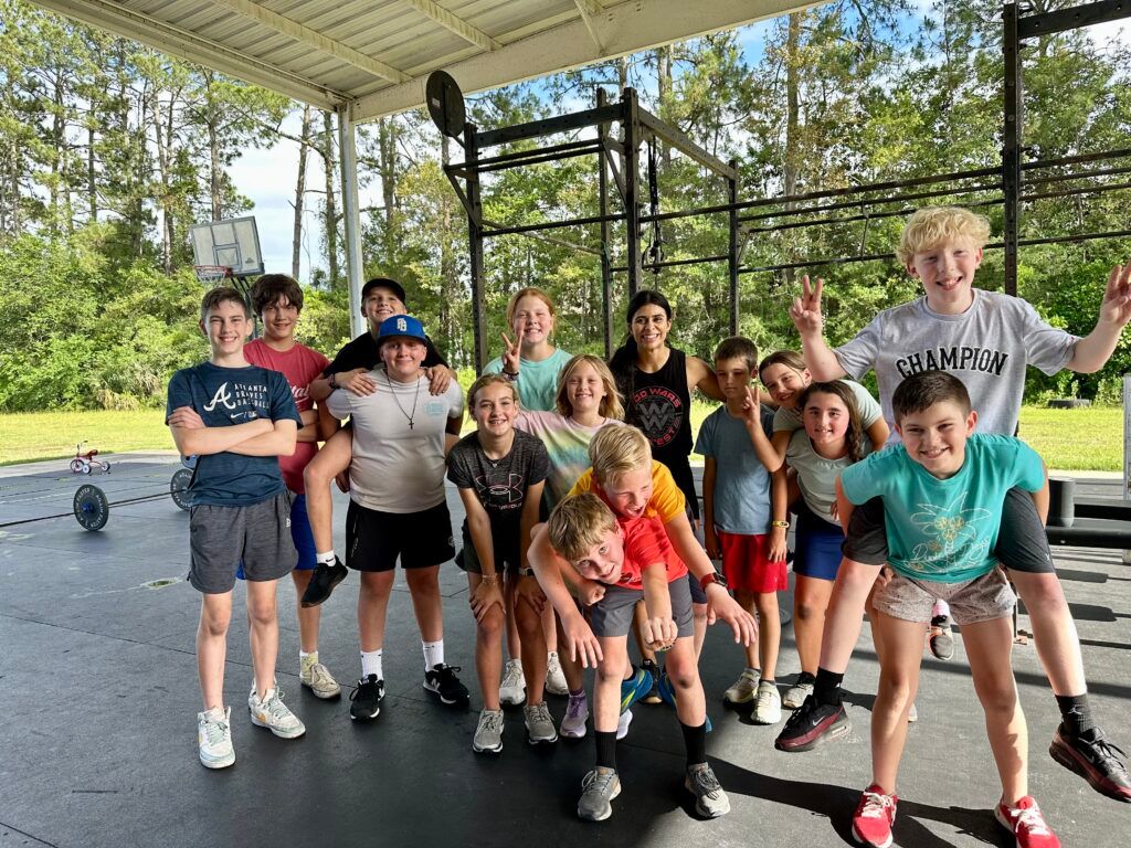 Group of people posing together in a covered outdoor gym, smiling and waving in casual sportswear.