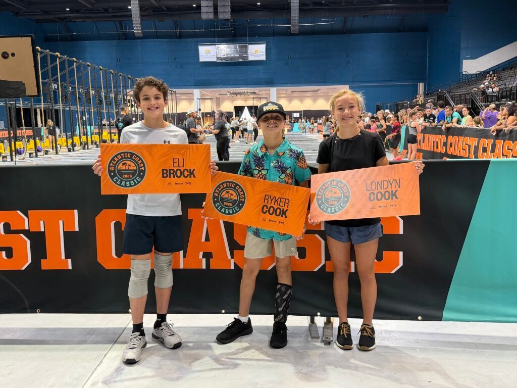 Three people holding orange signs at an indoor sports event, with a crowd in the background.