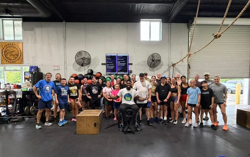 Large group posing in CrossFit Fernandina in Yulee,FL, with a barbell, wooden box, and fans on the wall.