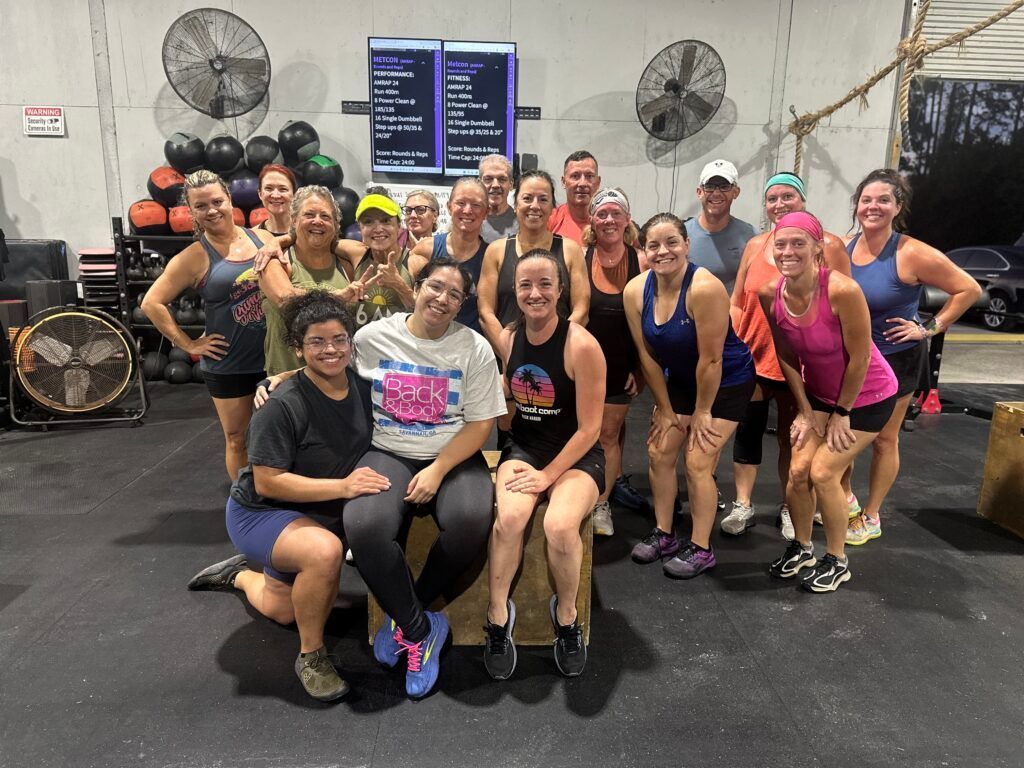 Group fitness class posing together in CrossFit Fernandina in Yulee,FL, smiling in front of fans and workout equipment.