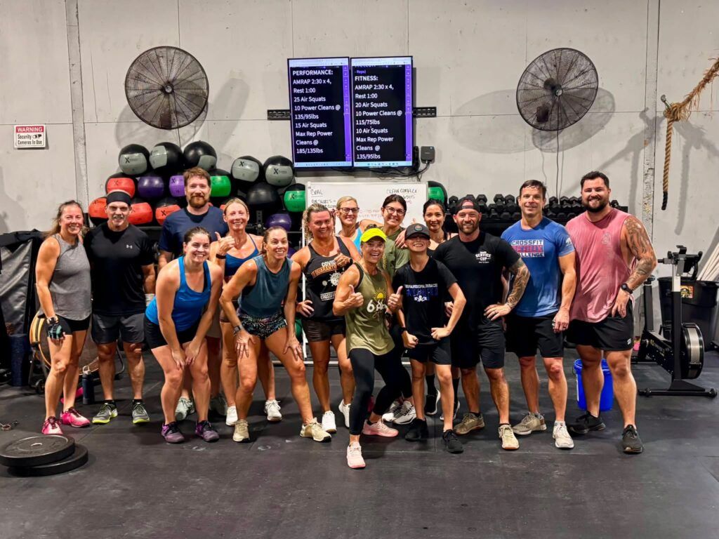 Group of people posing together in CrossFit Fernandina in Yulee,FL, smiling with kettlebells and barbells in the background