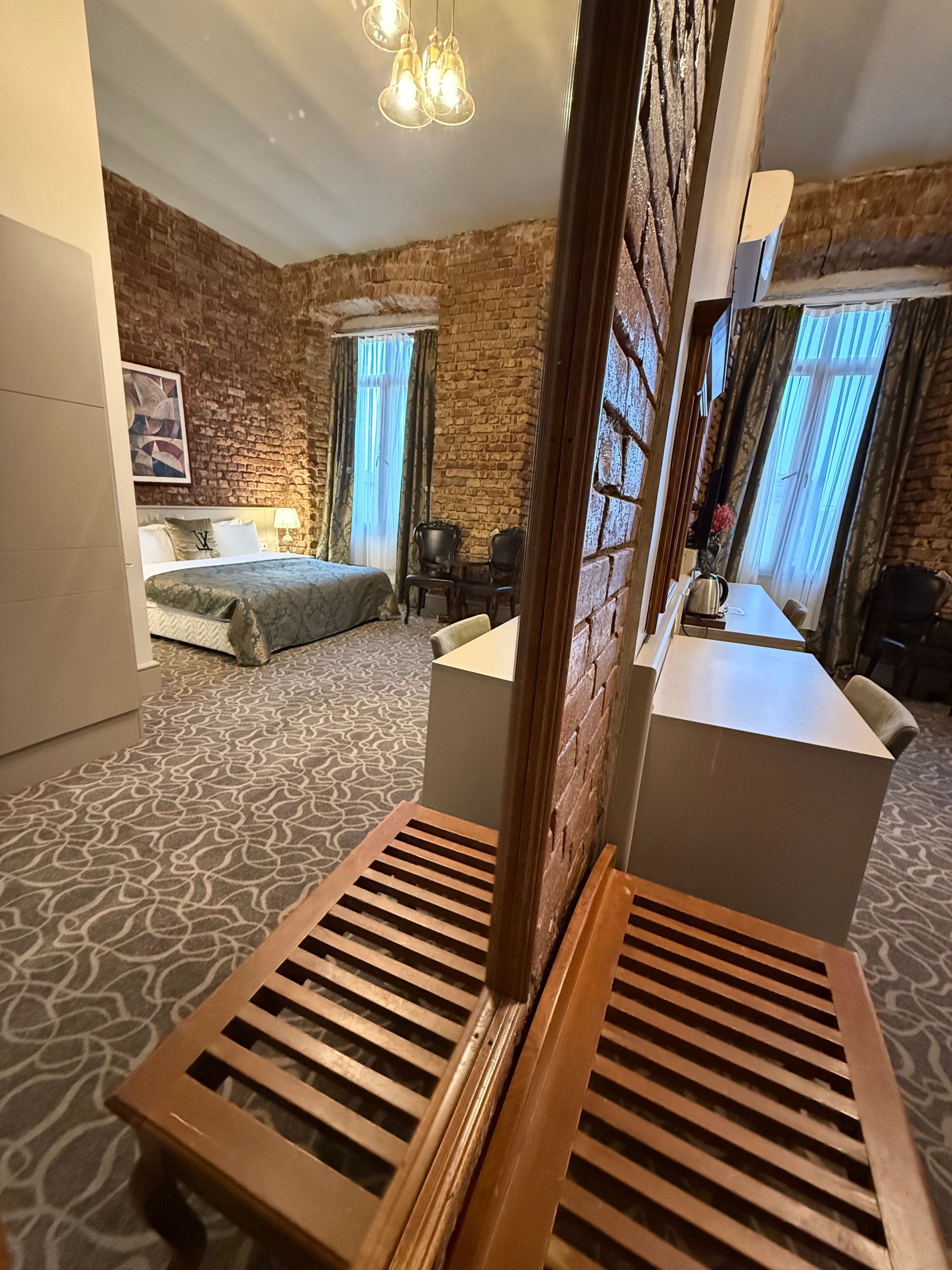 A hotel room with a patterned carpet, a central wooden privacy screen, a bed near a window, and a desk area.