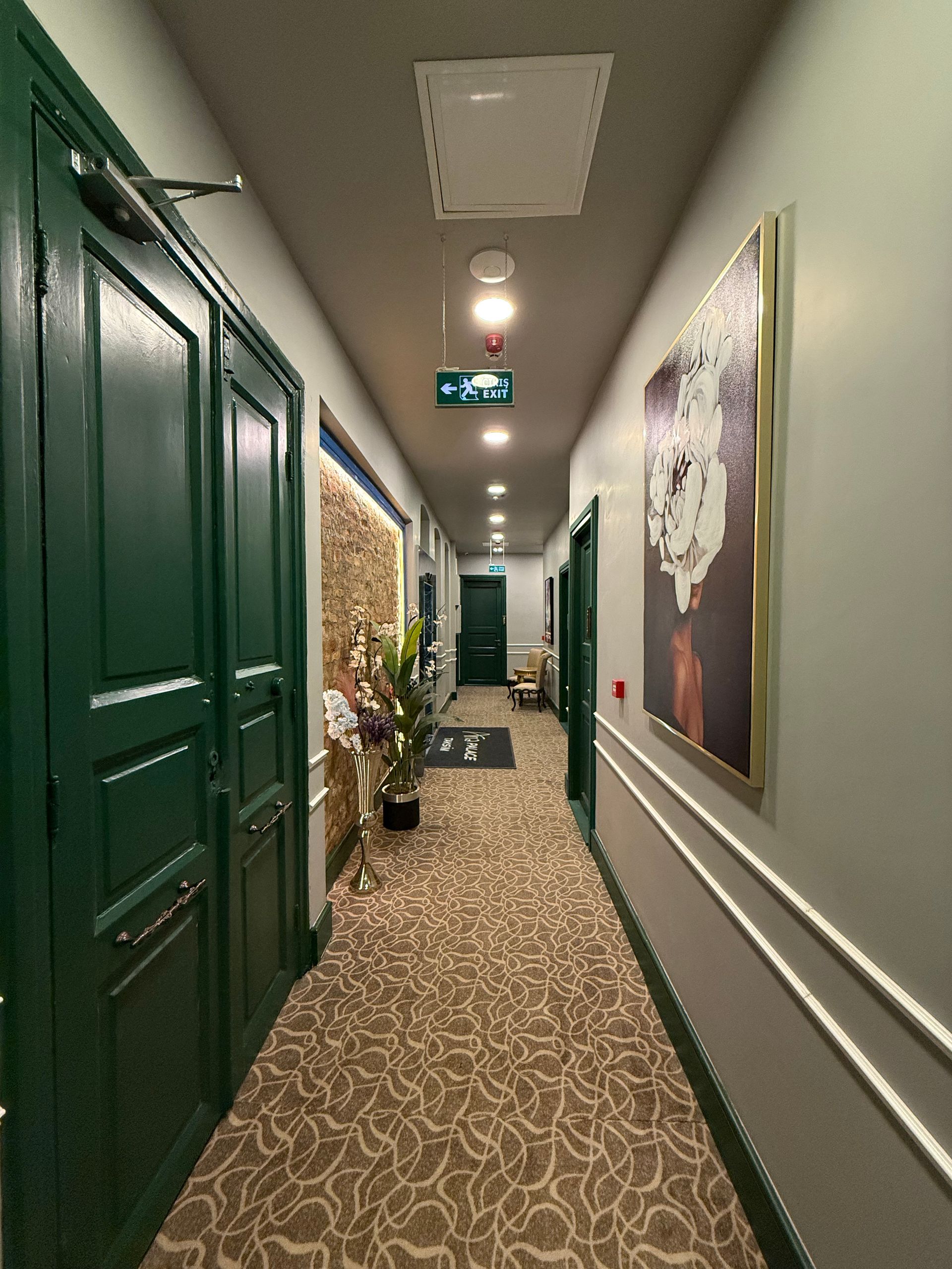 A long hotel corridor with green doors on the left, patterned carpet, wall molding, and framed art on the right.