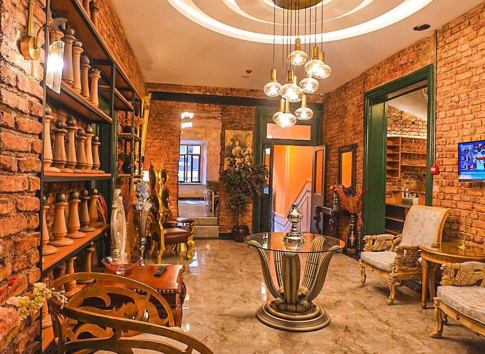 A cozy hotel lobby with exposed brick walls, a modern light fixture, ornate gold chairs, and a glass-topped table.