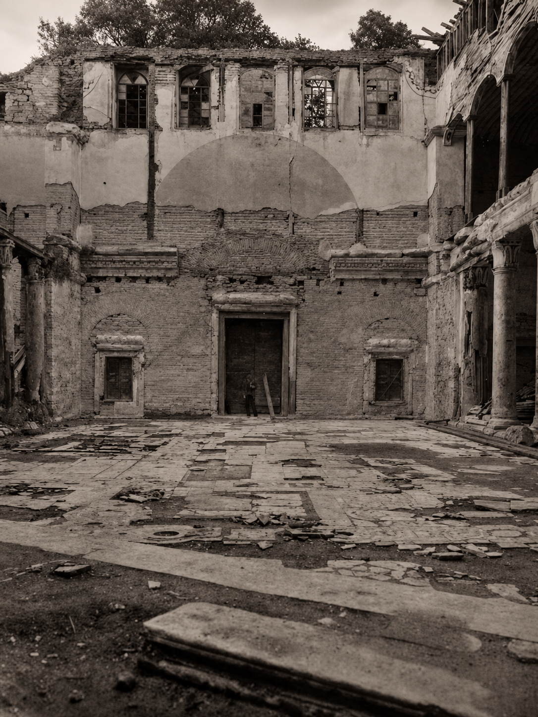 A black and white, eye-level view of the interior ruins of a historic stone building with a central arched doorway.