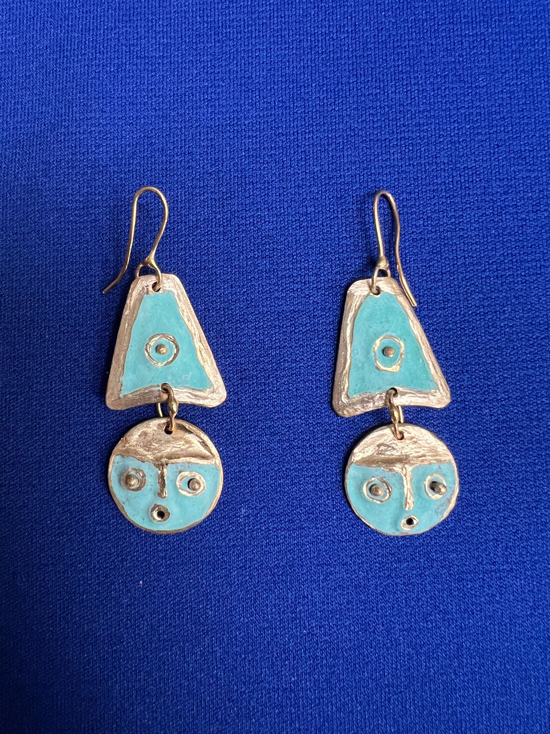 A pair of earrings with a face on them are sitting on a blue surface.
