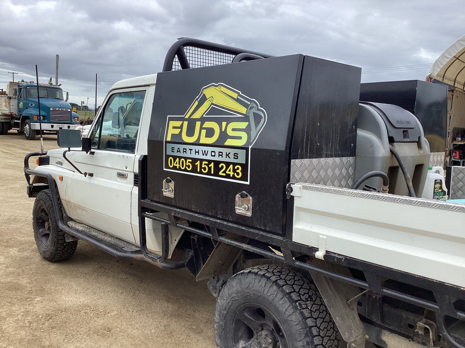 White utility truck with black storage box and FUD’S logo parked on a gravel lot under cloudy skies