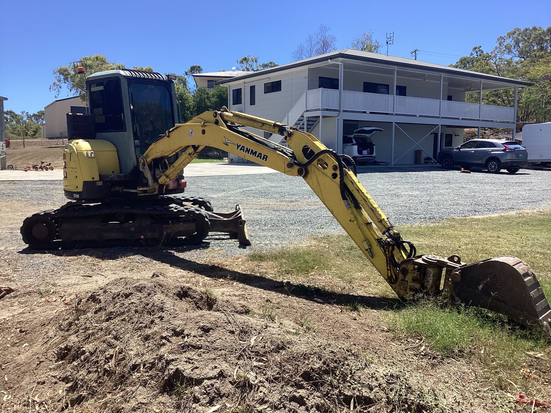 Yellow excavator digging dirt beside a building under a clear blue sky