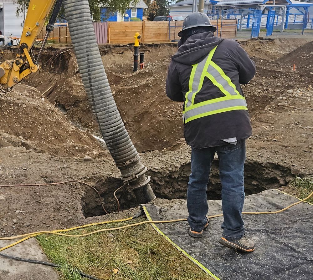 Worker in Reflective Vest Stands Beside Excavator Hose at a Muddy Construction Site — Fud's Concreting In Proserpine, QLD