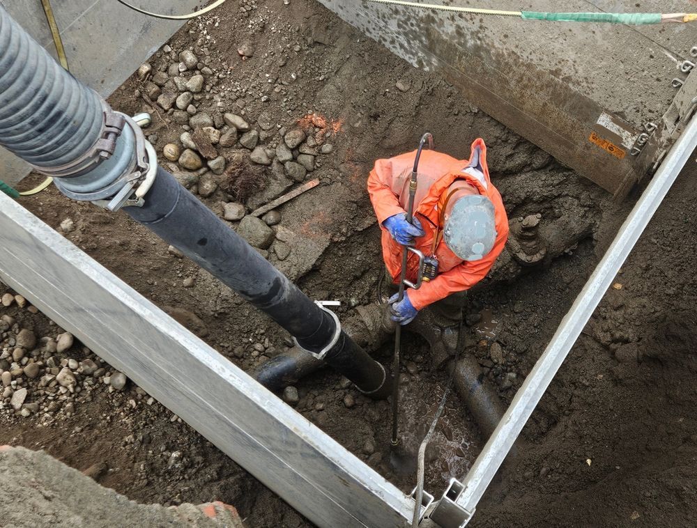 Worker in Orange Safety Gear Inspecting a Utility Trench Beside Pipes and Gravel — Fud's Concreting In Proserpine, QLD