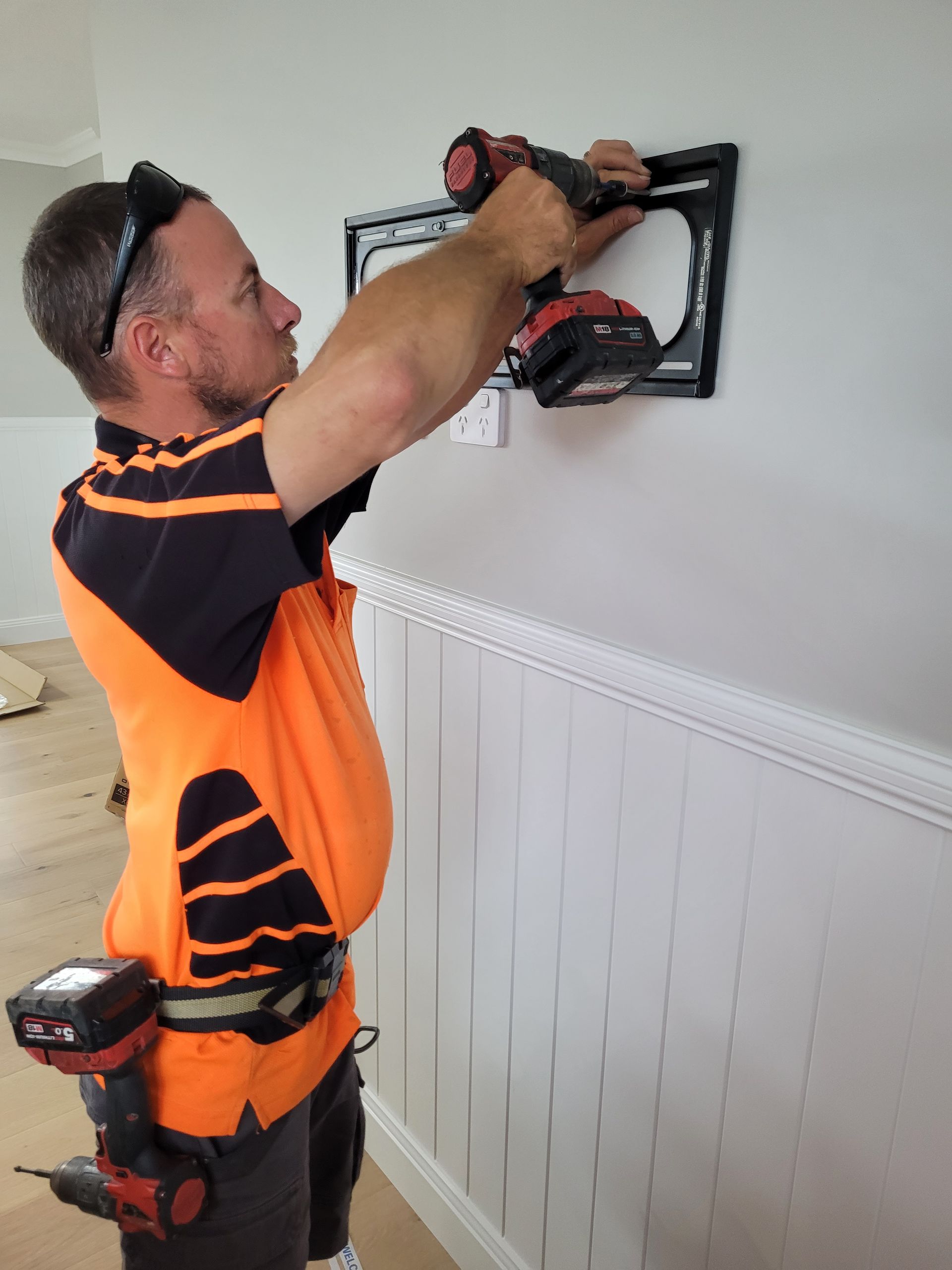 A Man is Using a Drill to Install a Frame on a Wall— Brisbane Antenna Specialists in Brendale, QLD