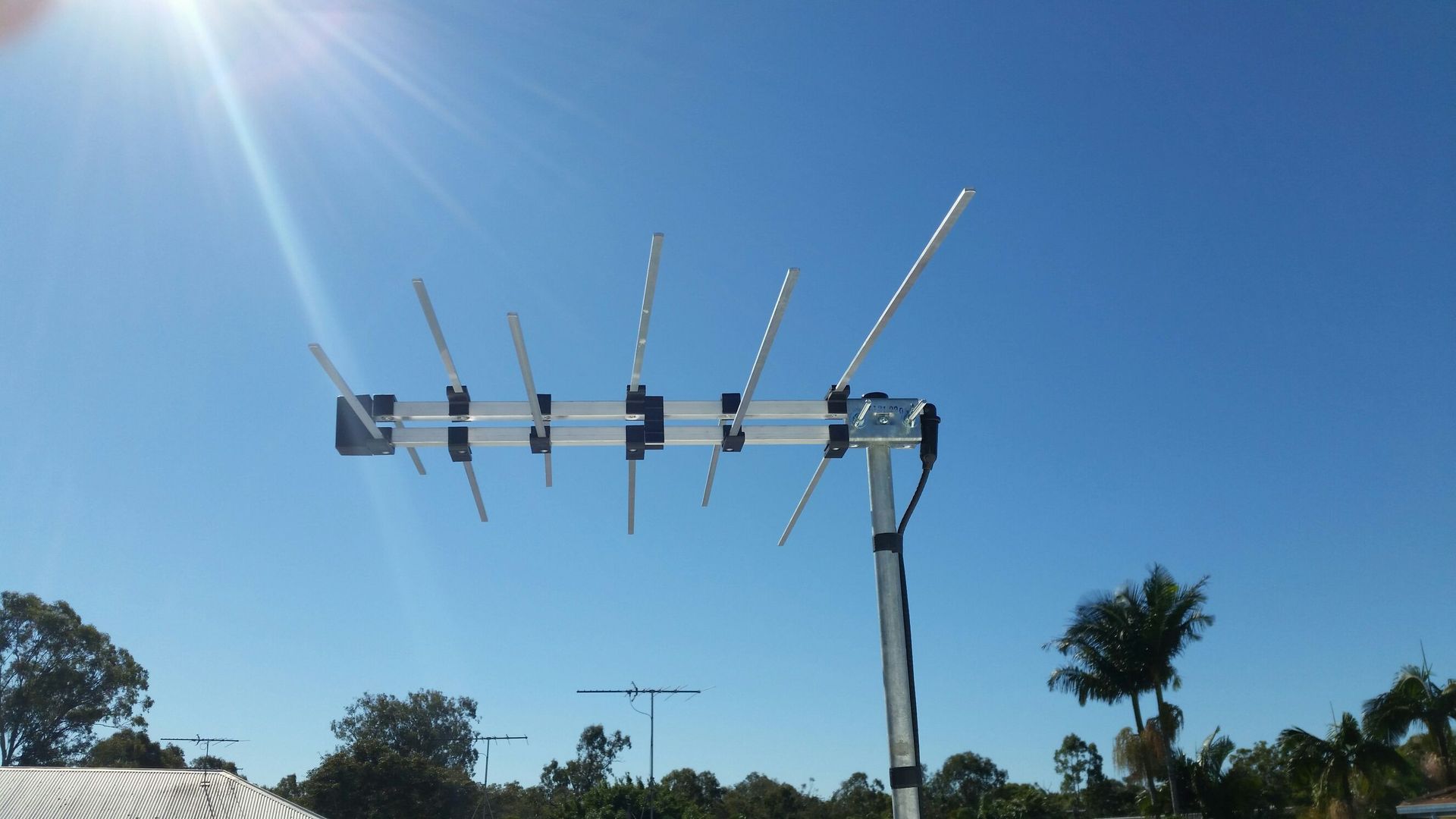 A Large Antenna Against a Blue Sky With Trees in the Background — Brisbane Antenna Specialists in Brendale, QLD