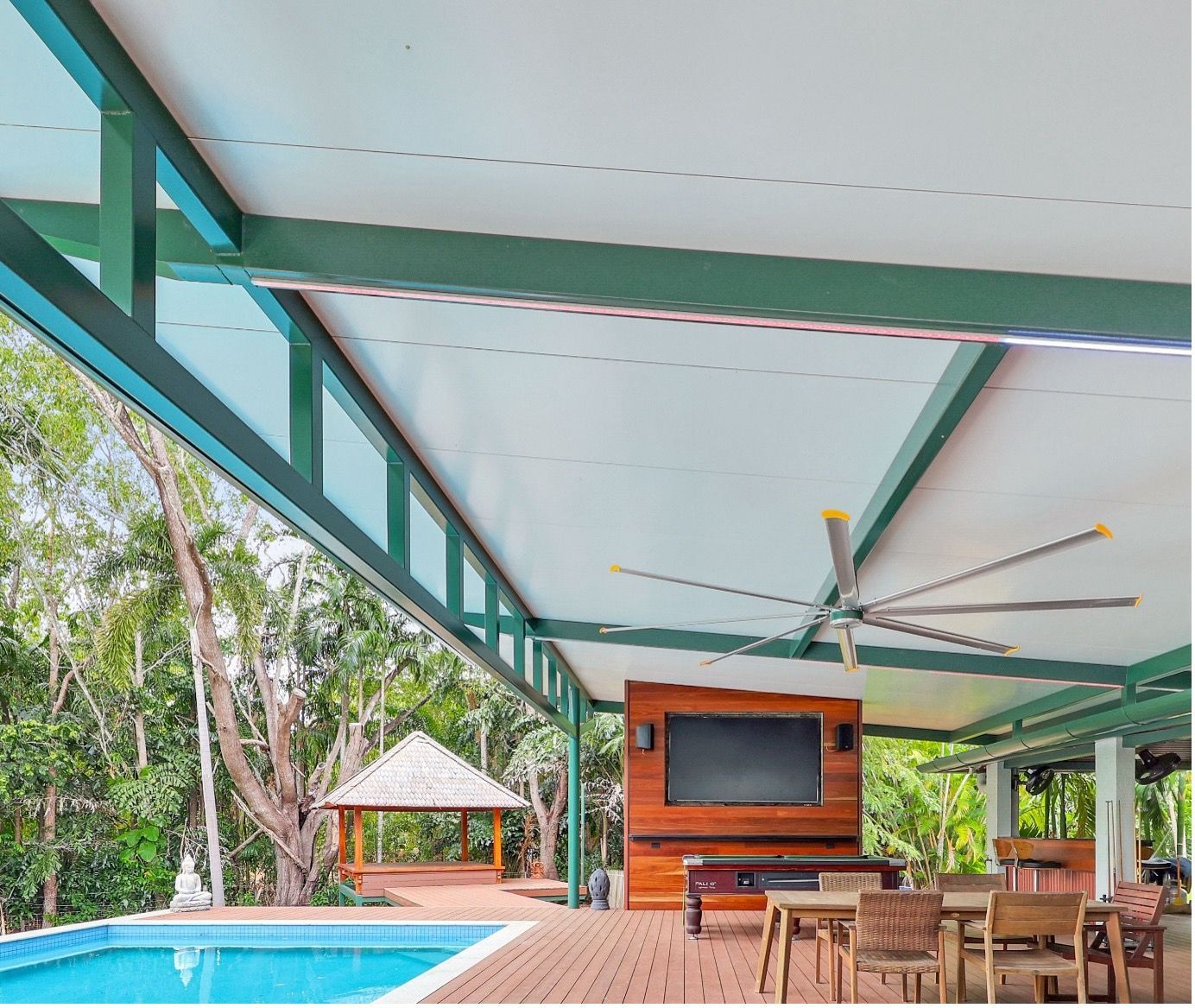 Covered poolside patio with turquoise beams, wooden dining set, ceiling fan, and pool beside trees — Arctic Installations in Winnellie, NT