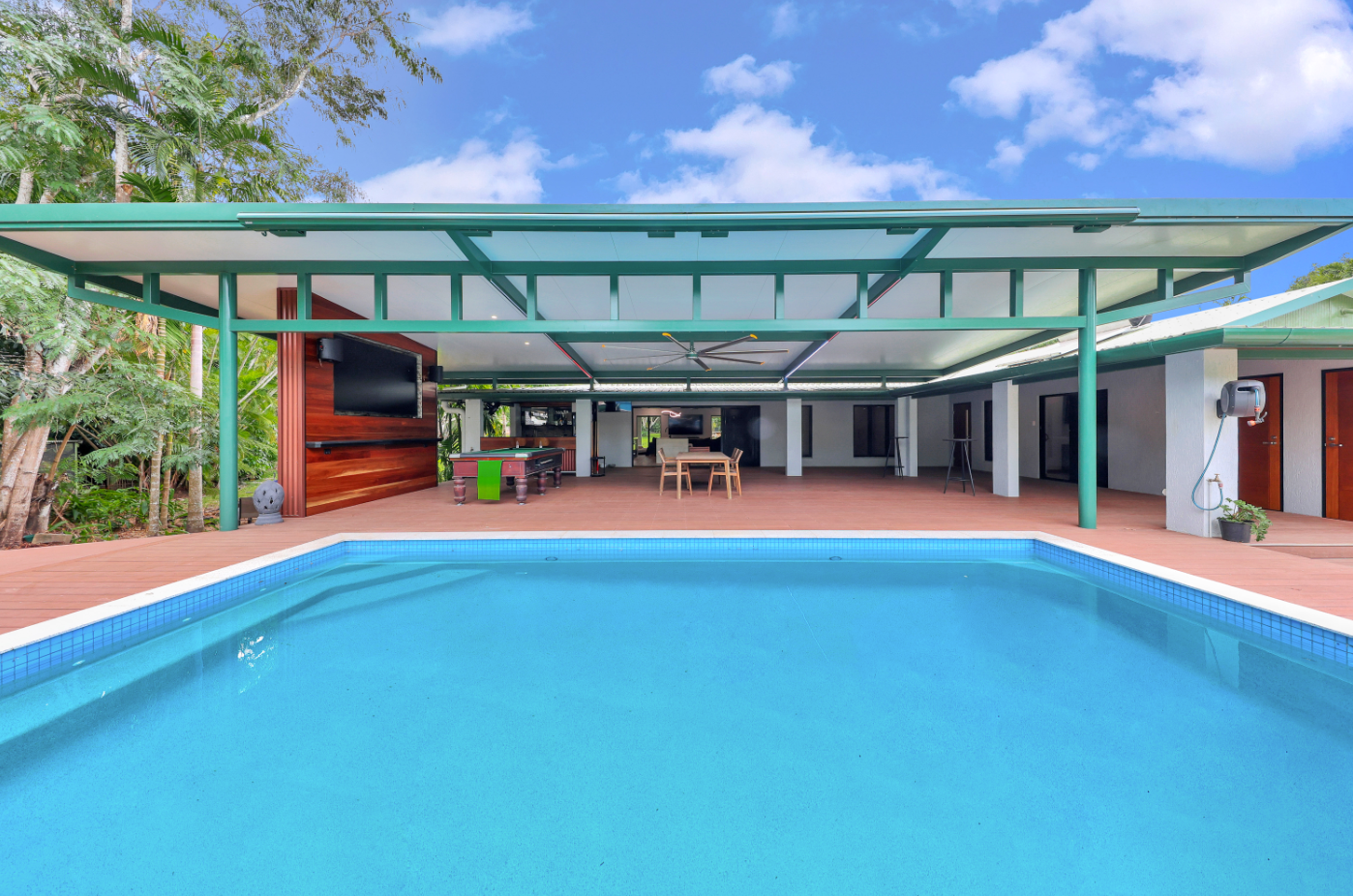 A large swimming pool in front of a house with a green roof.