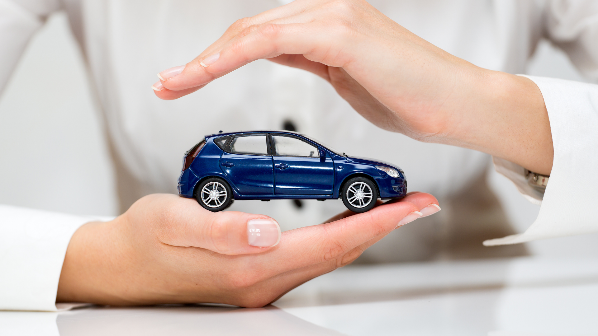 A person holding a small blue car model in their hands, symbolizing the protection and care provided through insurance for vehicle repairs.