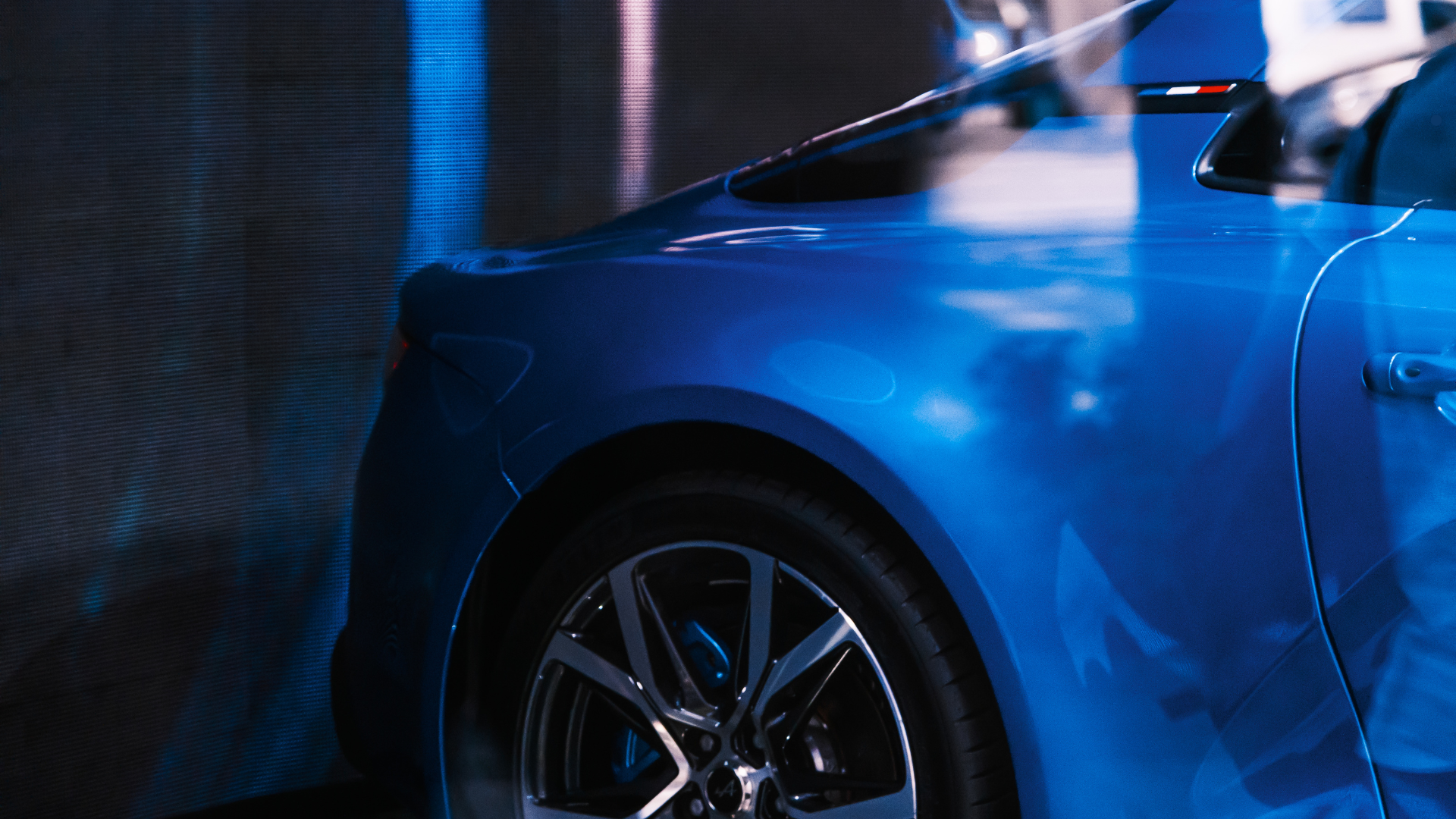 Close-up of a blue car front quarter panel in a body shop showing surface reflections and repair preparation under lighting