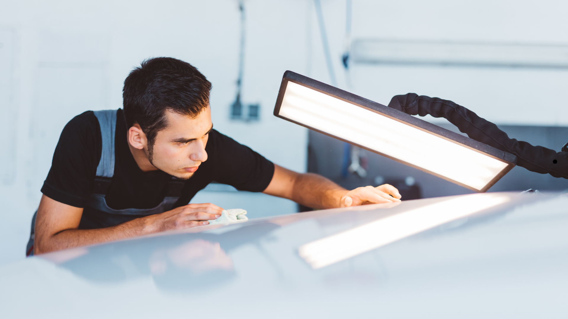 Auto technician inspecting vehicle panel for dents using a specialized LED light during paintless dent removal service.