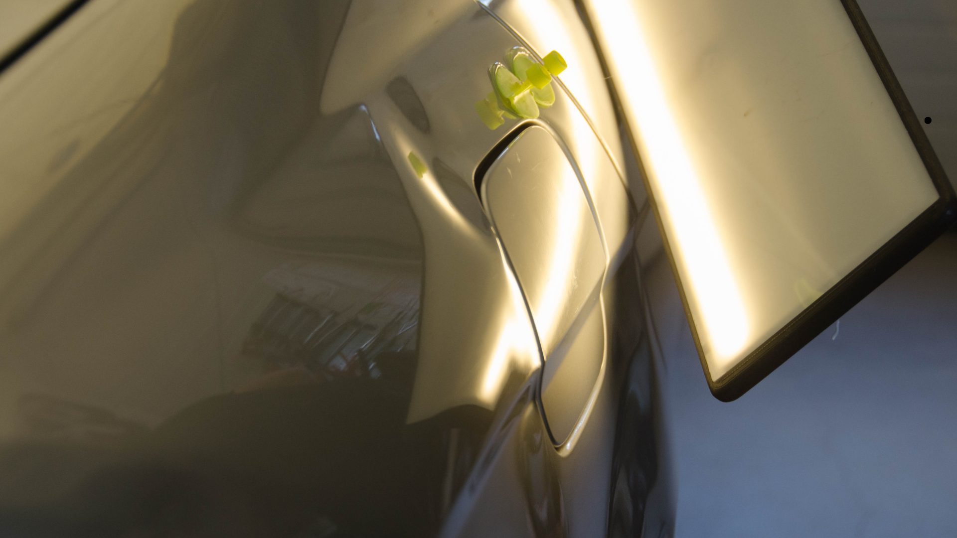 Close-up of vehicle body panel reflecting inspection light, revealing dent areas during paintless de