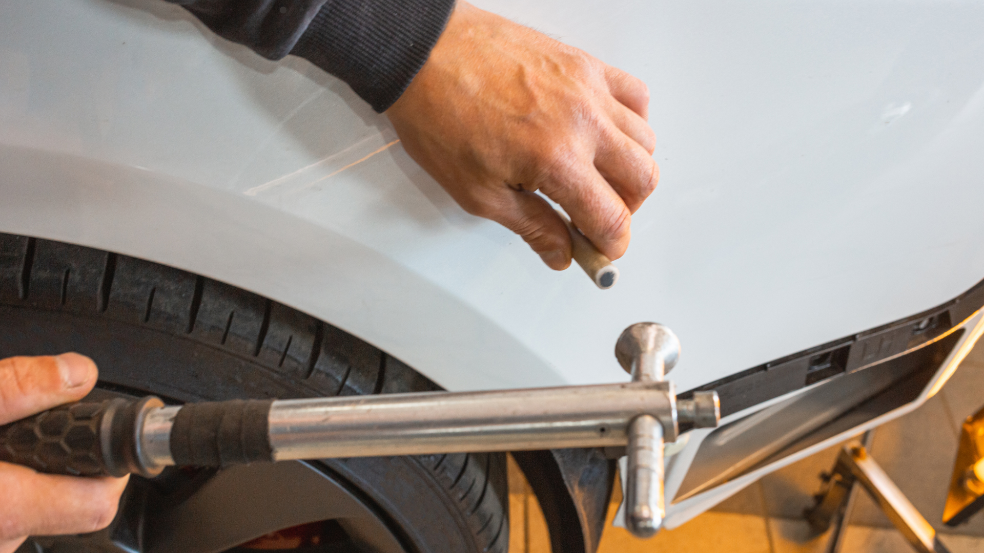 A professional using a tool to inspect the grey paint of a Mercedes-Benz car in a workshop.