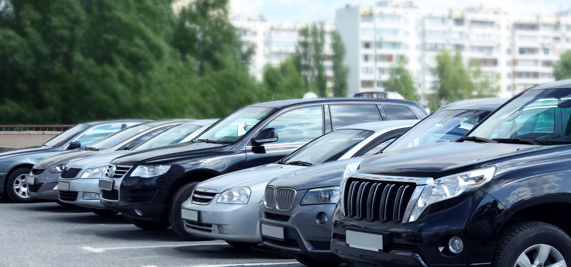 Row of parked black and silver SUVs in a lot, front view with trees and buildings in the background