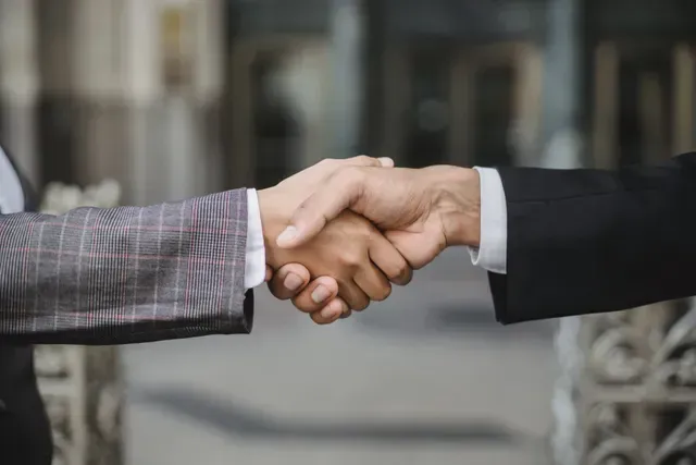 Two people shaking hands, likely sealing a deal, outdoors.