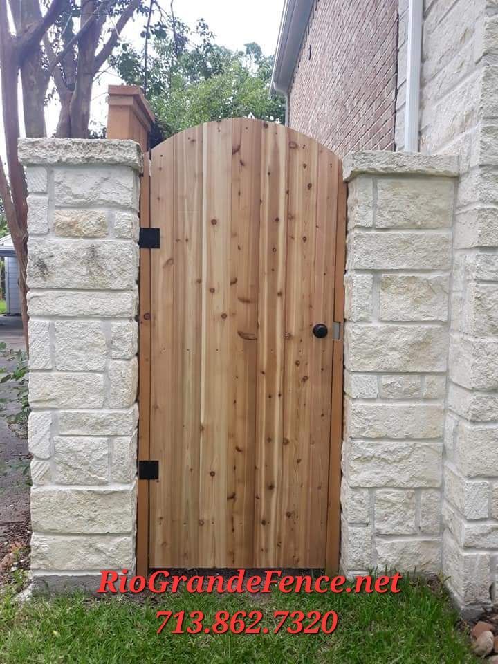 A Wooden Gate Is Between Two Stone Pillars in Front of A House - Houston, TX - Rio Grande Fence Company