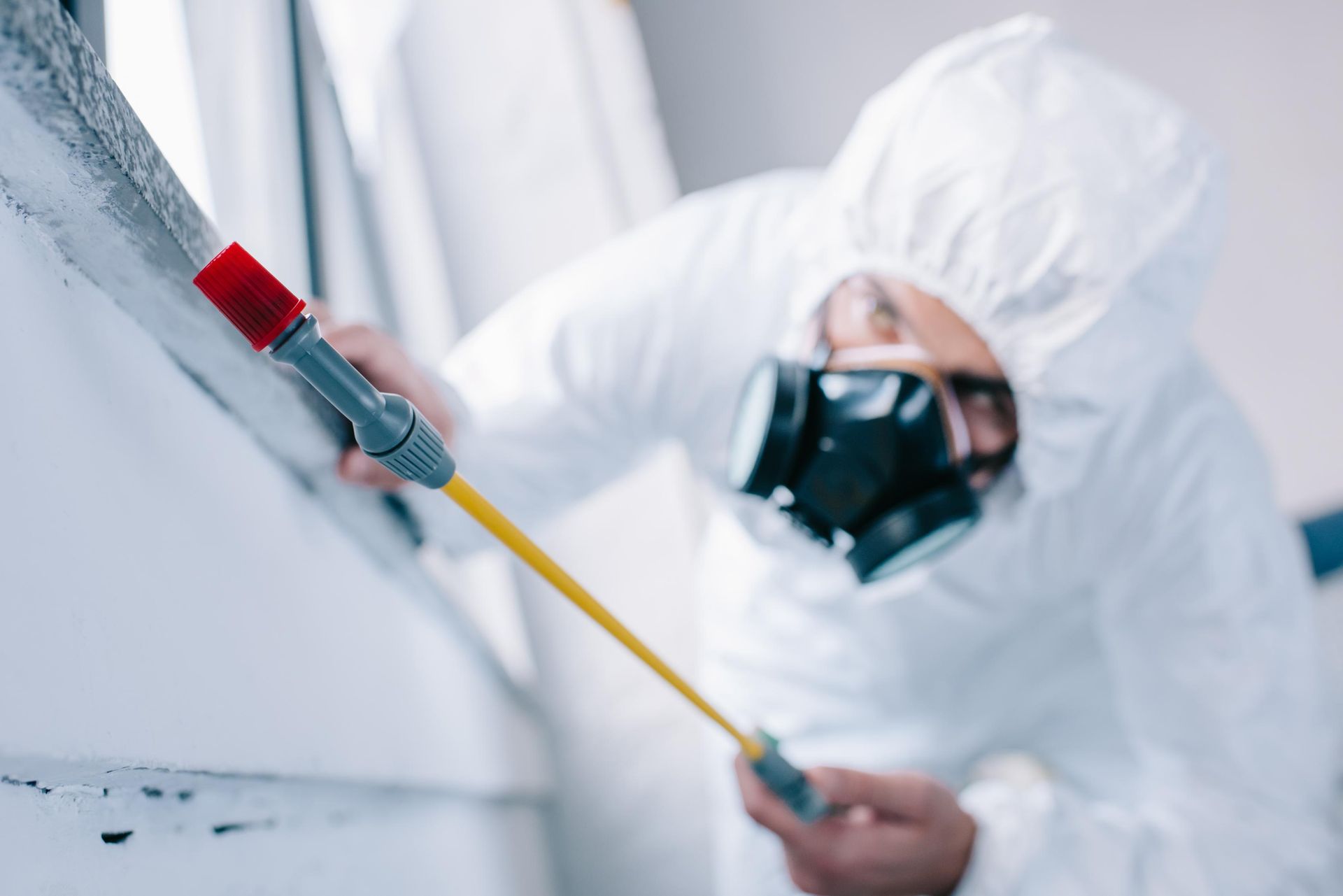 A man in a protective suit is spraying a wall with a sprayer.
