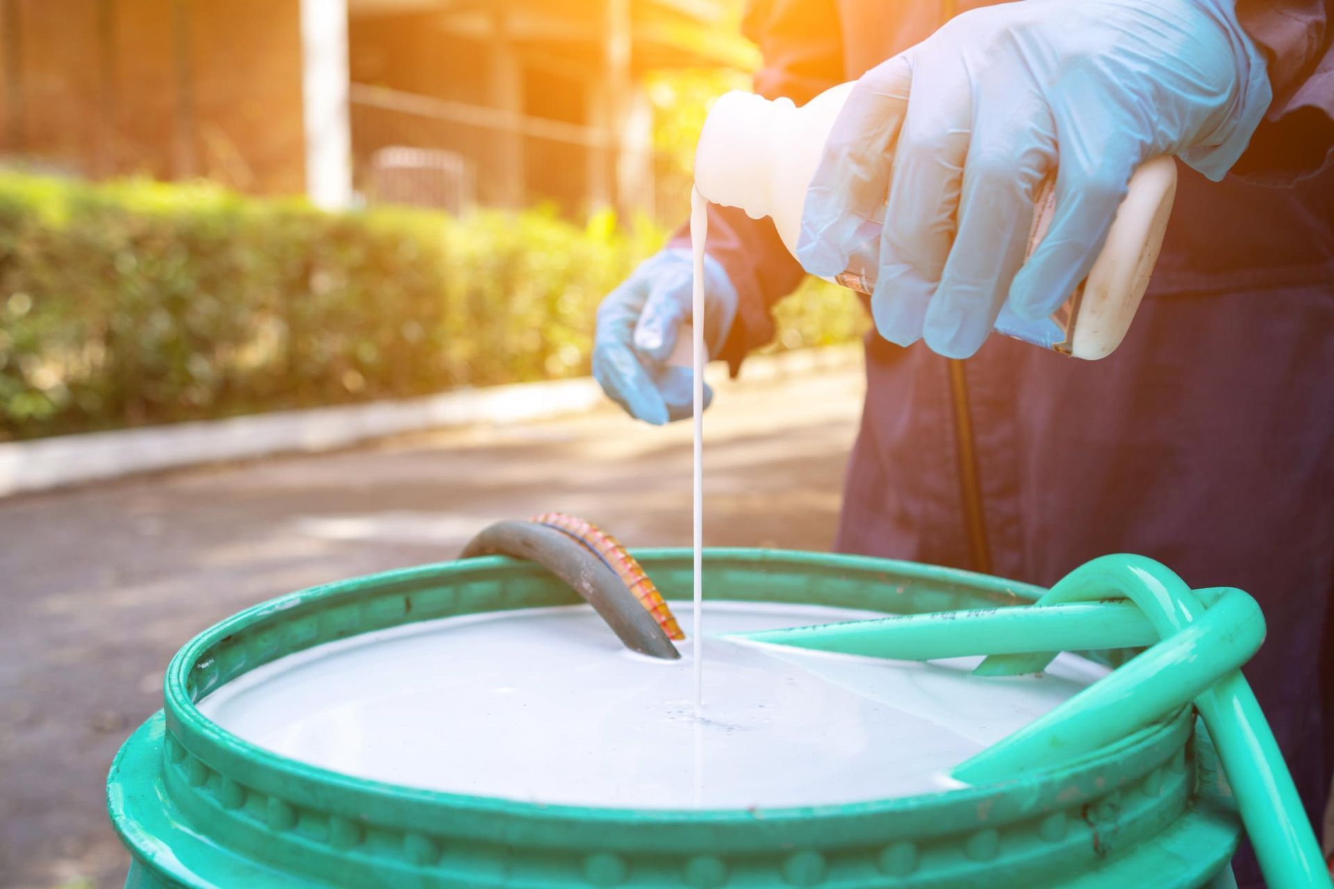 A person is pouring a bottle of liquid into a green bucket.