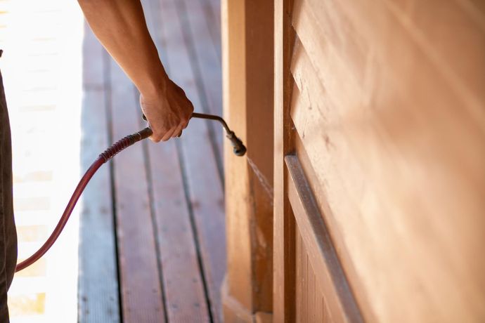 A person is spraying a wooden wall with a hose.