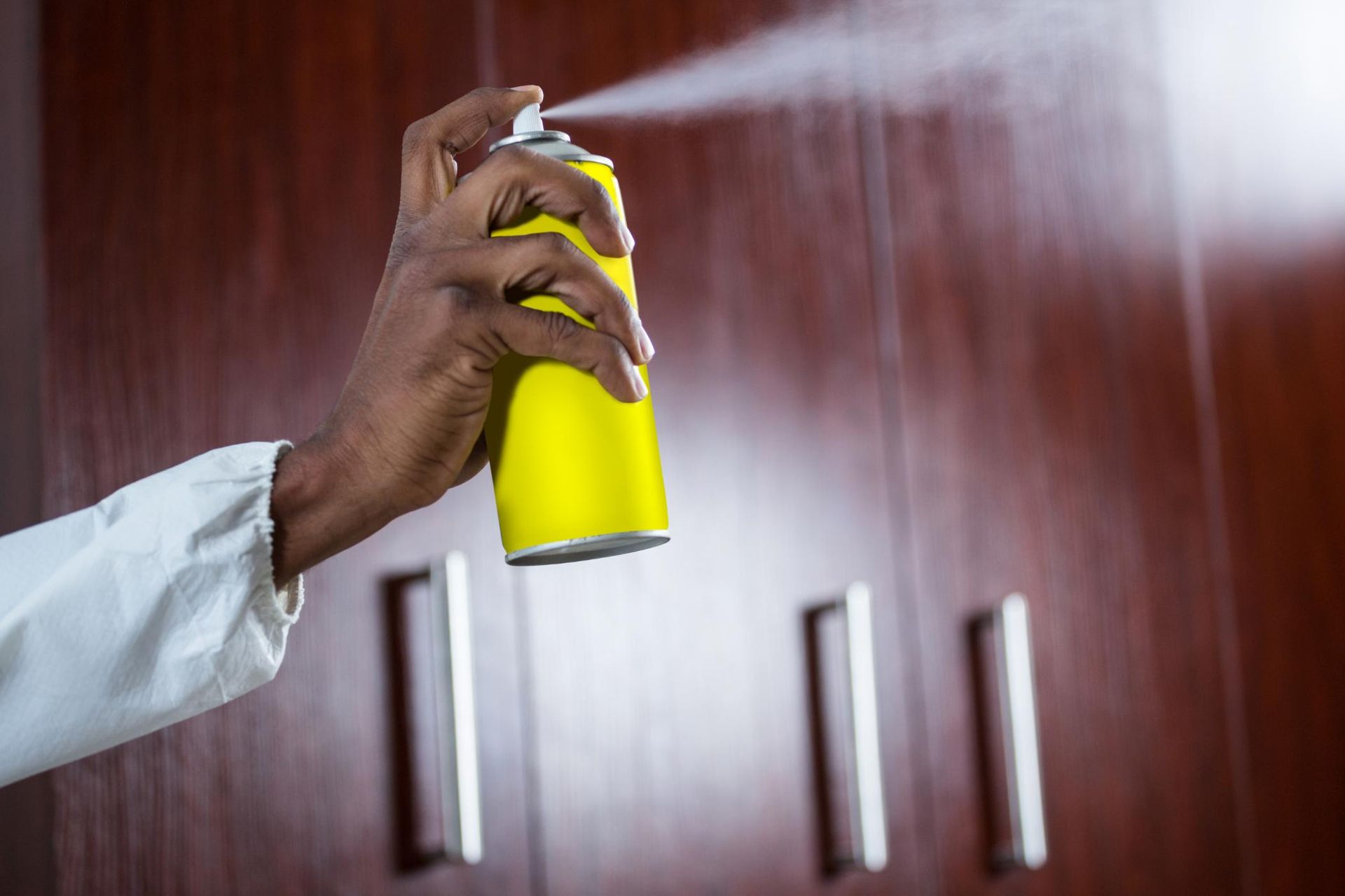 A person is spraying a can of spray on a wooden cabinet.