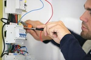 A man is working on an electrical box with a screwdriver.