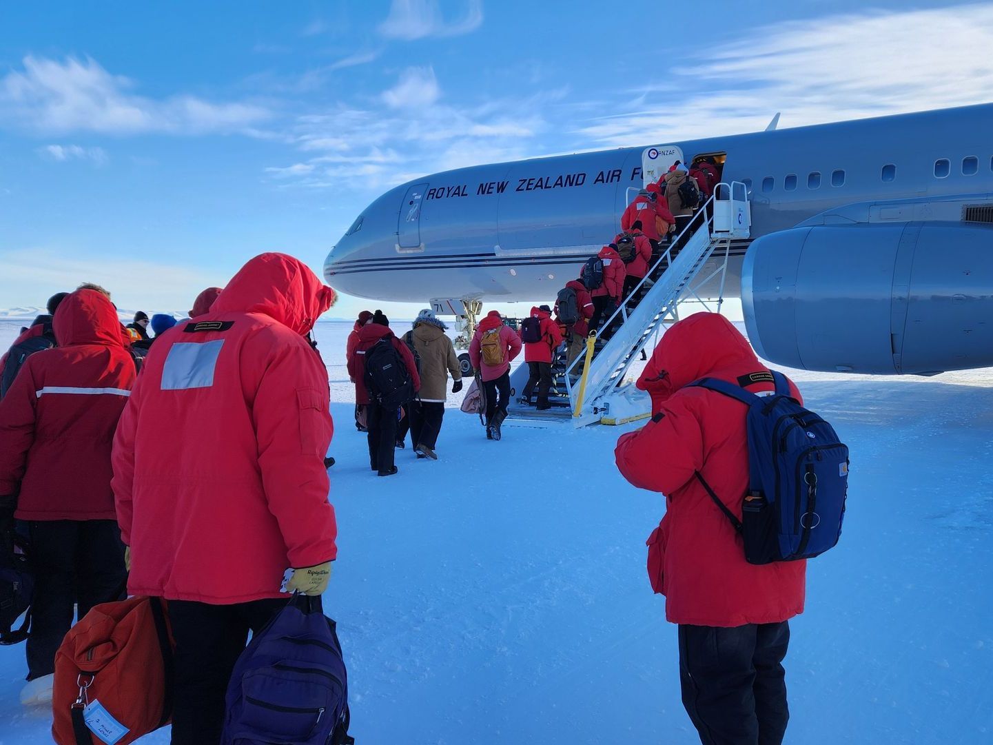 A group of people in red jackets in the snow are boarding an airplane