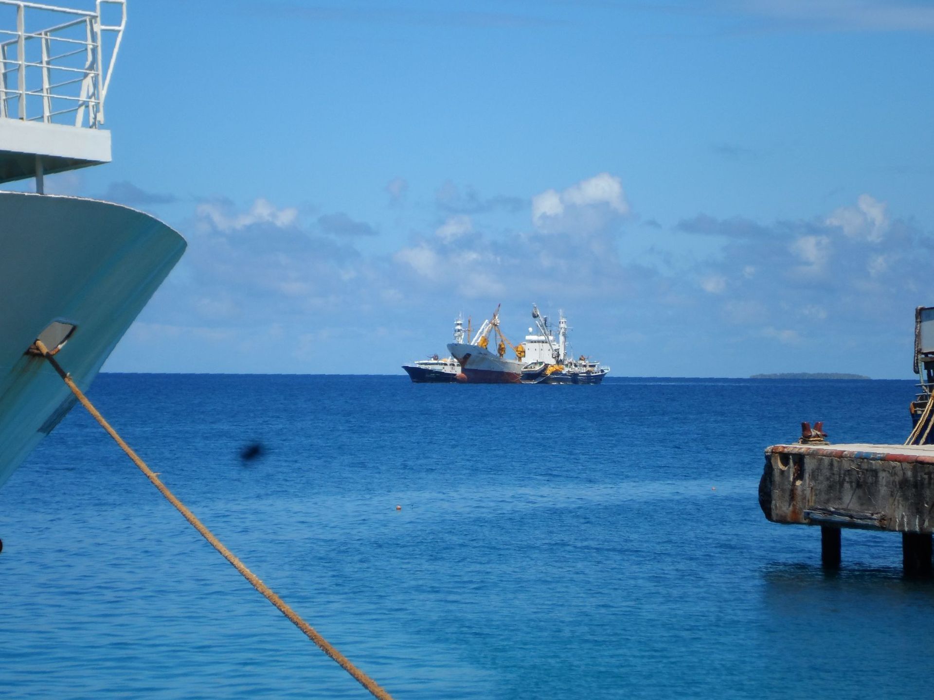 A boat is tied to a dock in the ocean, another boat is visible in the distance