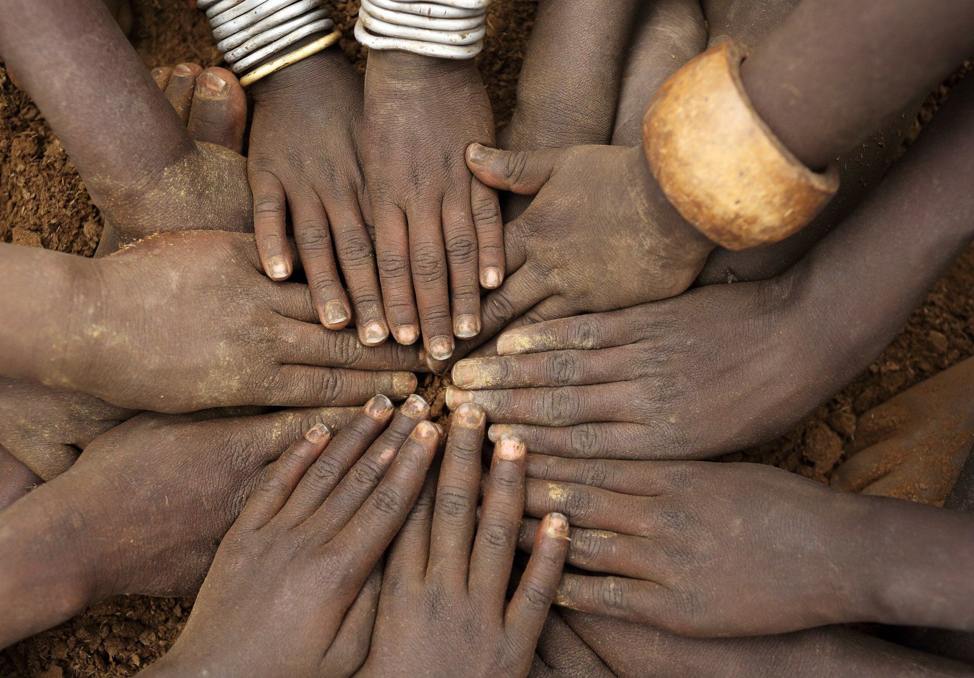 Many hands stacked in a circle on brown earth, symbolizing teamwork and unity