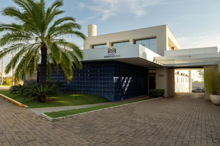 Prédio moderno com parede de tijolos azuis, palmeira e entrada para uma área fechada.