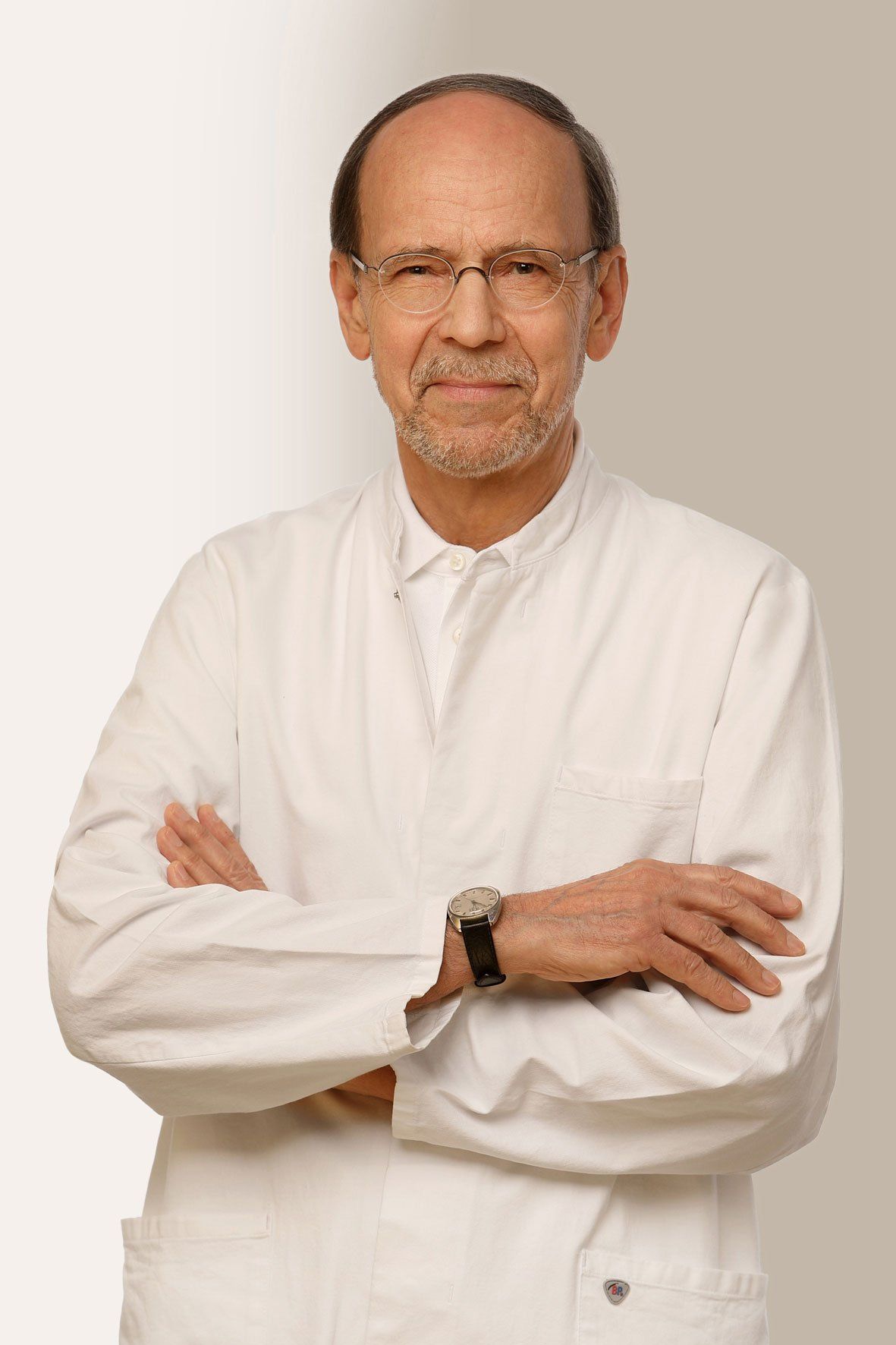 Gözlüklü, sakallı, kollarını kavuşturmuş, beyaz önlüklü doktor.
