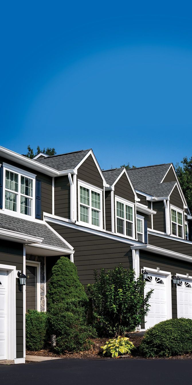 A row of dark-sided townhouses with white trim and grey shingled roofs under a clear blue sky.