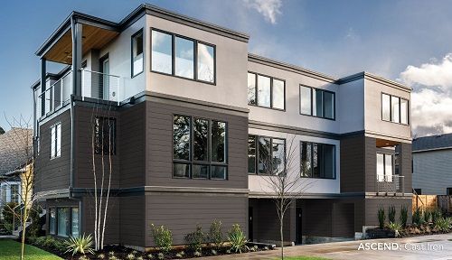 A modern three-story apartment building with dark brown lower panels, light grey upper levels, and multiple large windows.