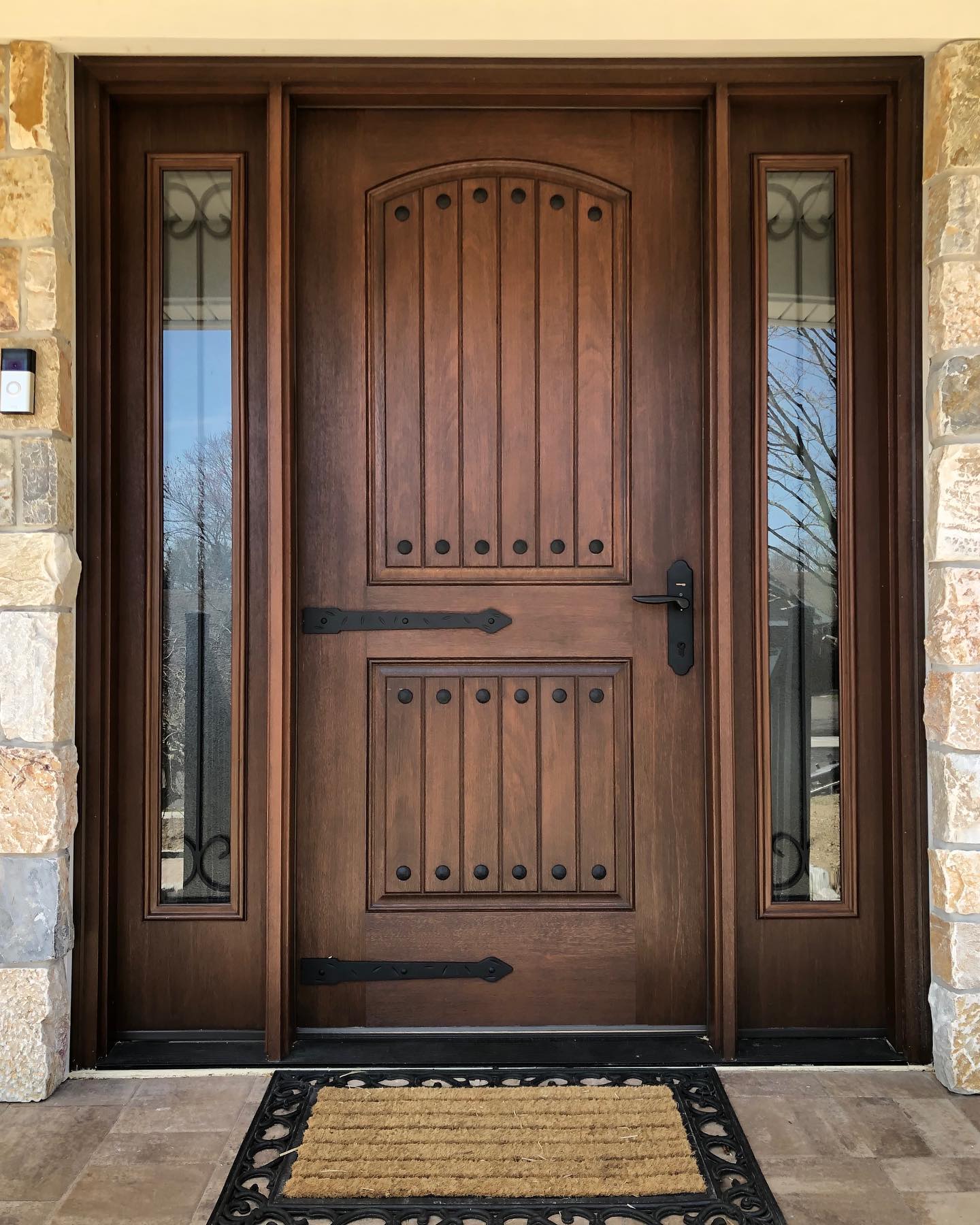 A dark wooden front door with vertical panels, decorative iron hinges, and sidelight windows with black metal accents.