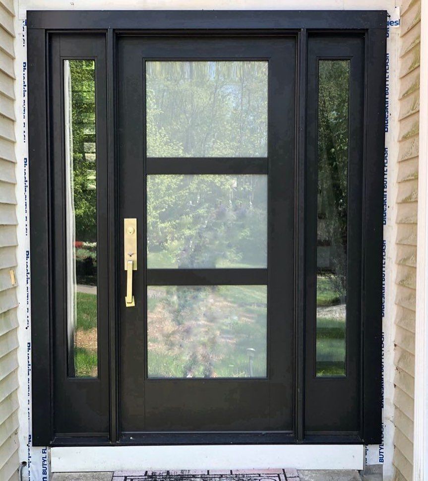 A modern black front door featuring three horizontal glass panels, flanked by two narrow vertical windows and a brass handle.