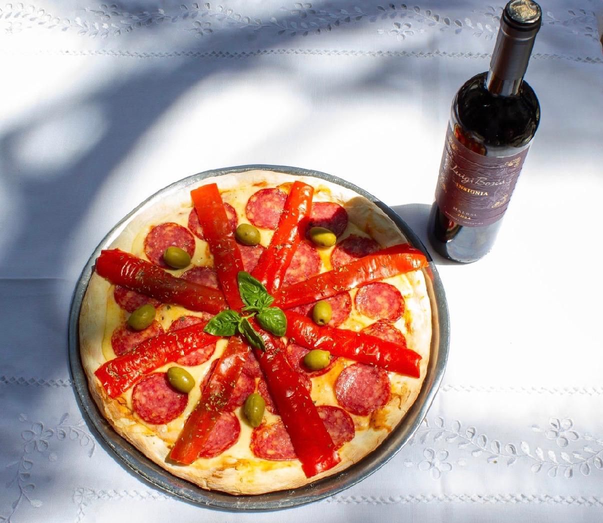 Una pizza grande de pepperoni y pimiento rojo asado en una bandeja de metal, con una tabla de madera