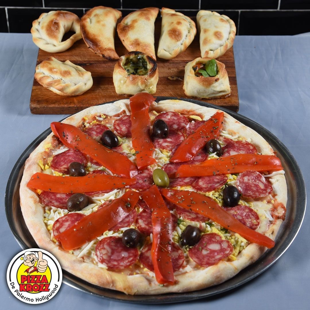 Una pizza de pepperoni con tiras de pimiento rojo y aceitunas