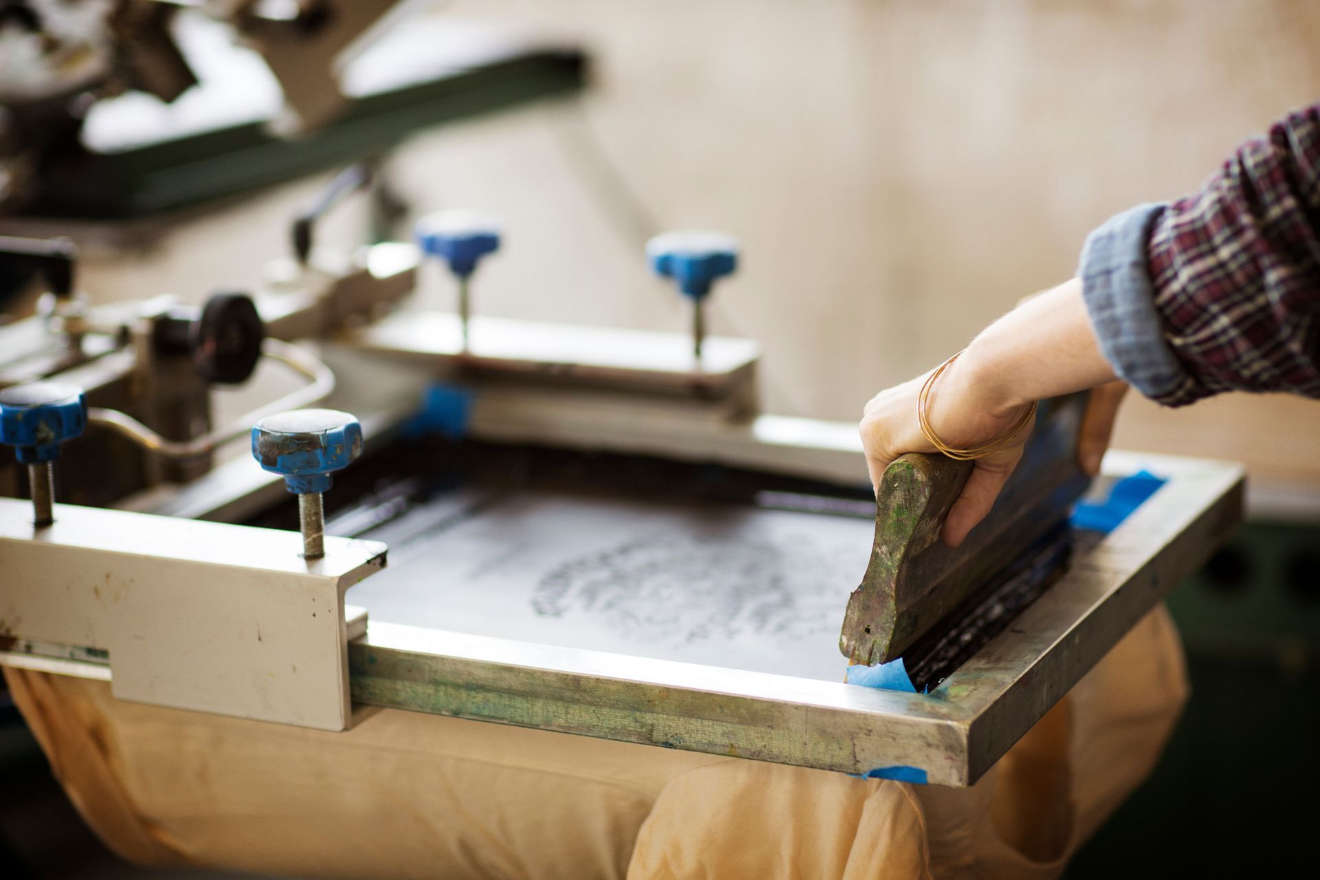 Cropped image of a woman performing screen printing on a workwear item at a workshop.