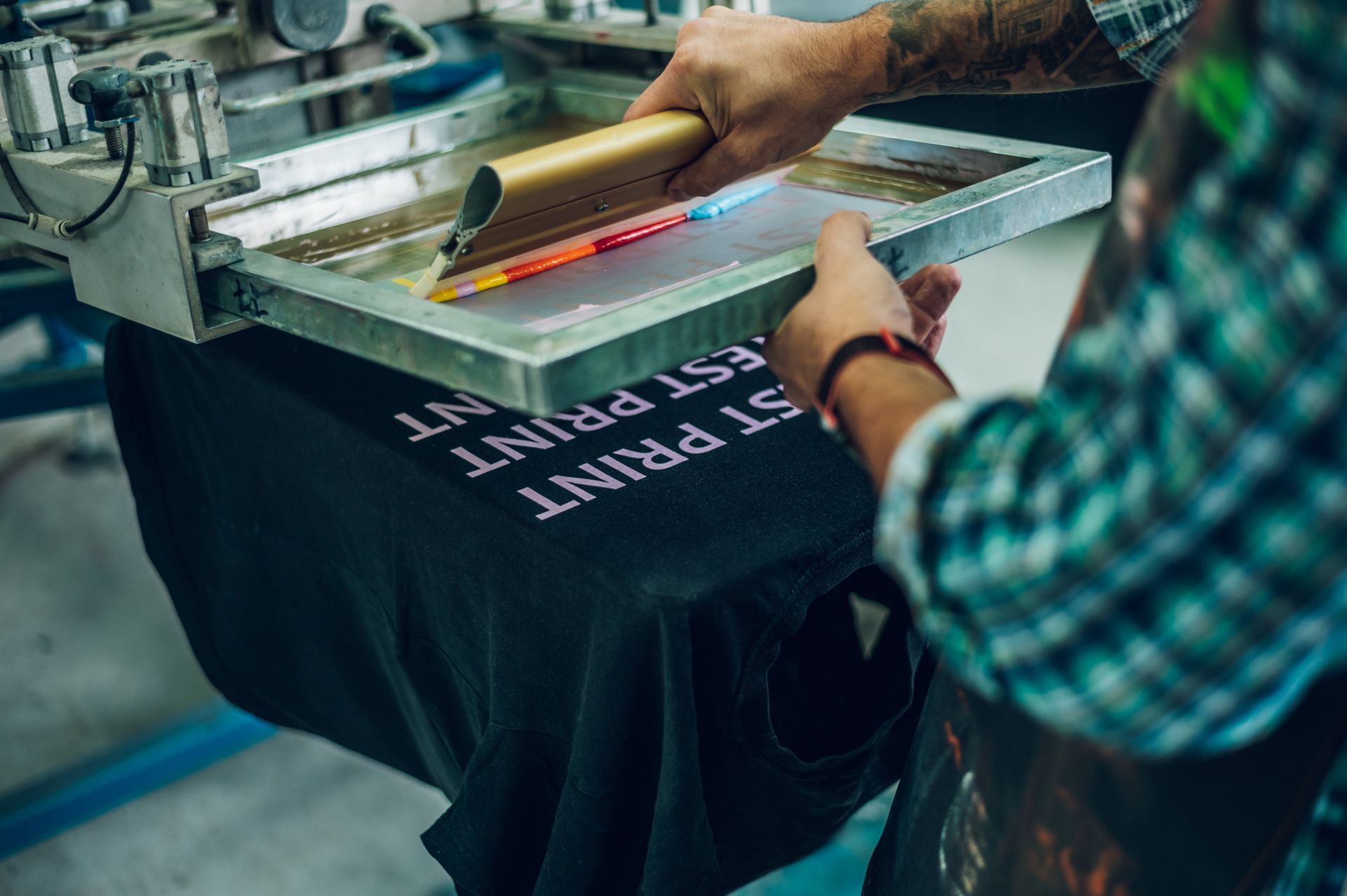 Close-up of a worker pressing ink on a frame while using the printing machine for custom workwear. Close-up of a worker pressing ink on a frame while using the printing machine for custom workwear.