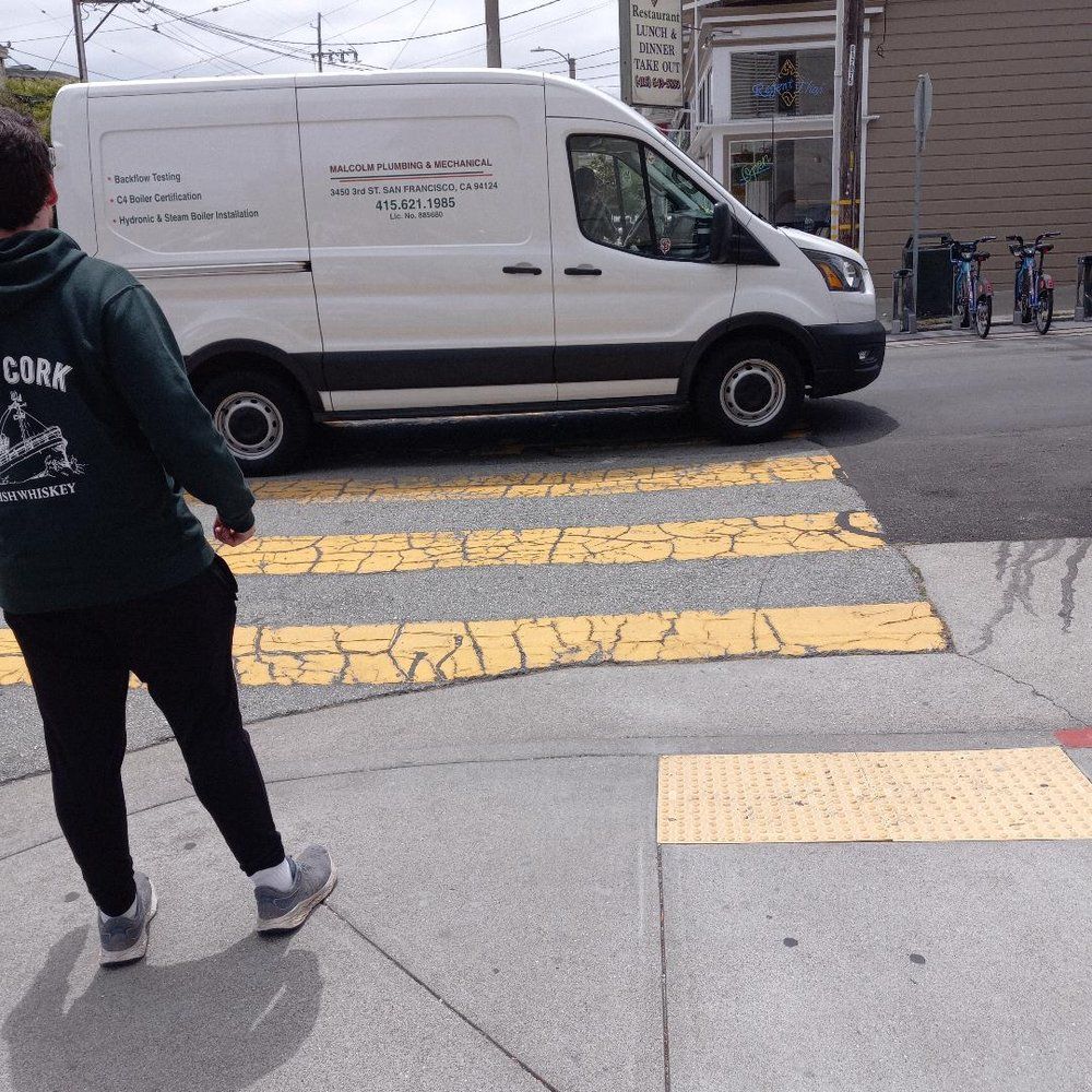 Person walking at a city crosswalk as a white van passes over yellow-striped pavement.