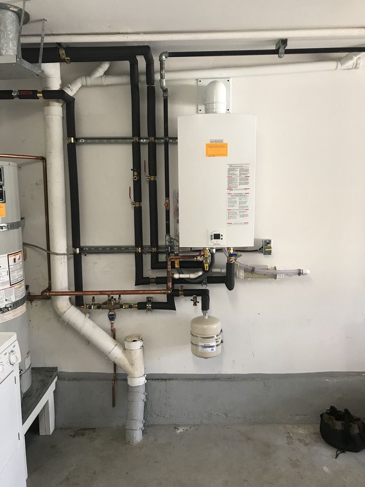 Utility room with white wall-mounted boiler, black pipes, and a water heater on a concrete floor