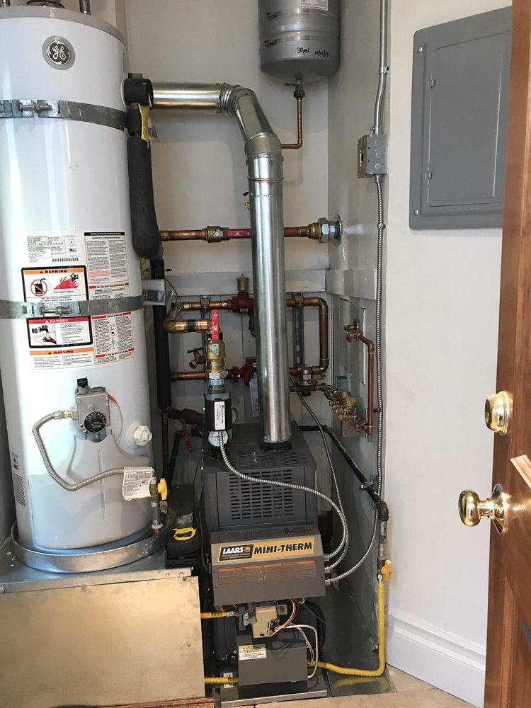 Water heater and boiler equipment with exposed pipes and control panels in a utility closet.