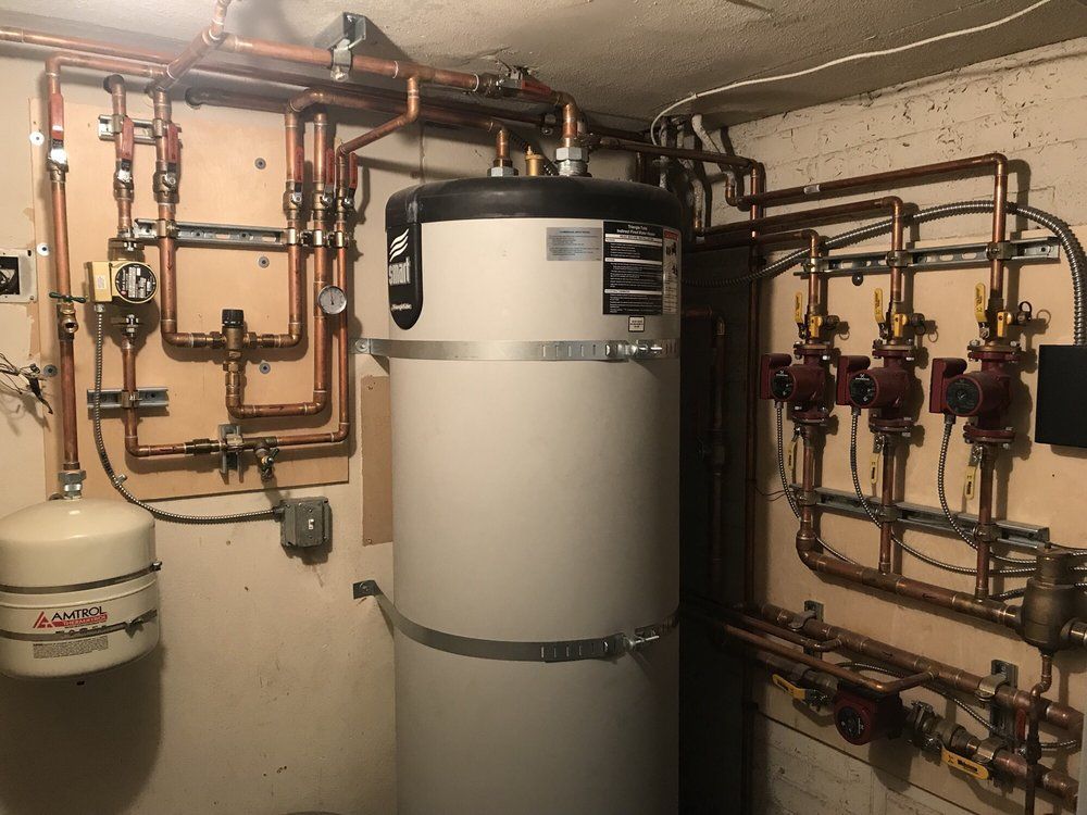 Boiler room with large white tank and exposed copper pipes and valves along the walls