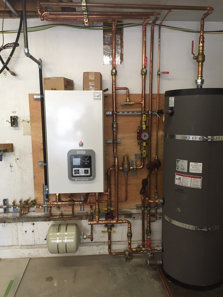 Boiler room with white wall-mounted unit, black water heater, exposed copper pipes, and tank on the floor